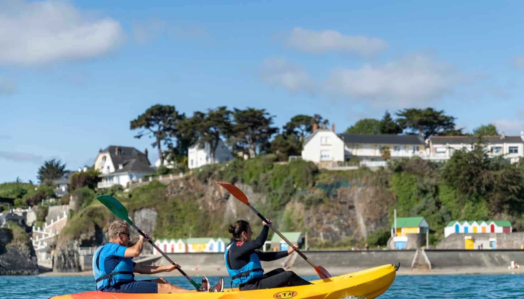 Kayakers naviguant près de la côte à Binic, Étables-sur-Mer, avec vue sur les maisons et la nature e.
